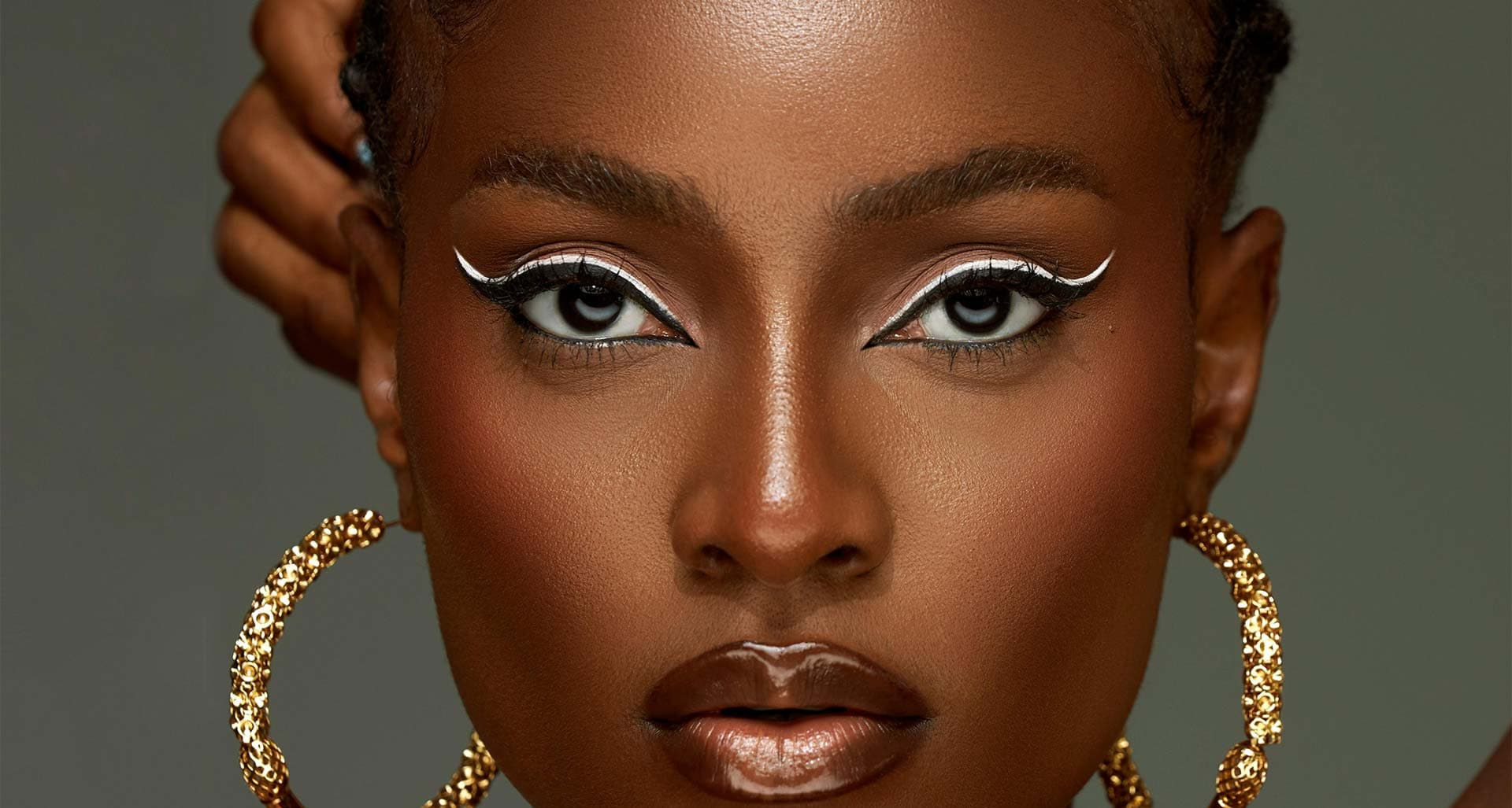 Regard souligné d'un trait blanc graphique, boucles d'oreilles dorées