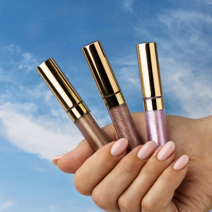 Trois gloss tenus dans une main, ciel en fond